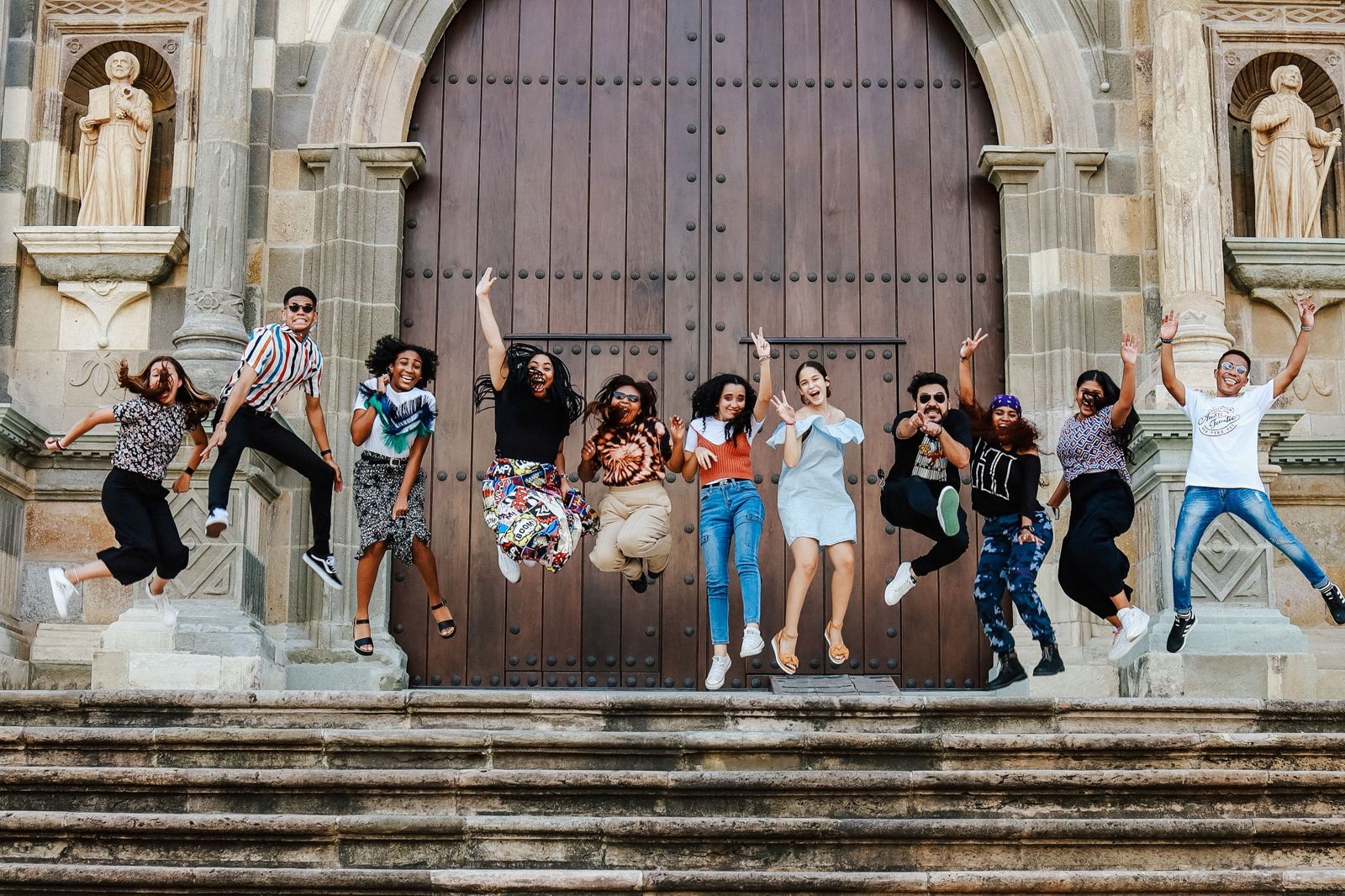 A group of young people jumping for joy on the steps of a historic cathedral