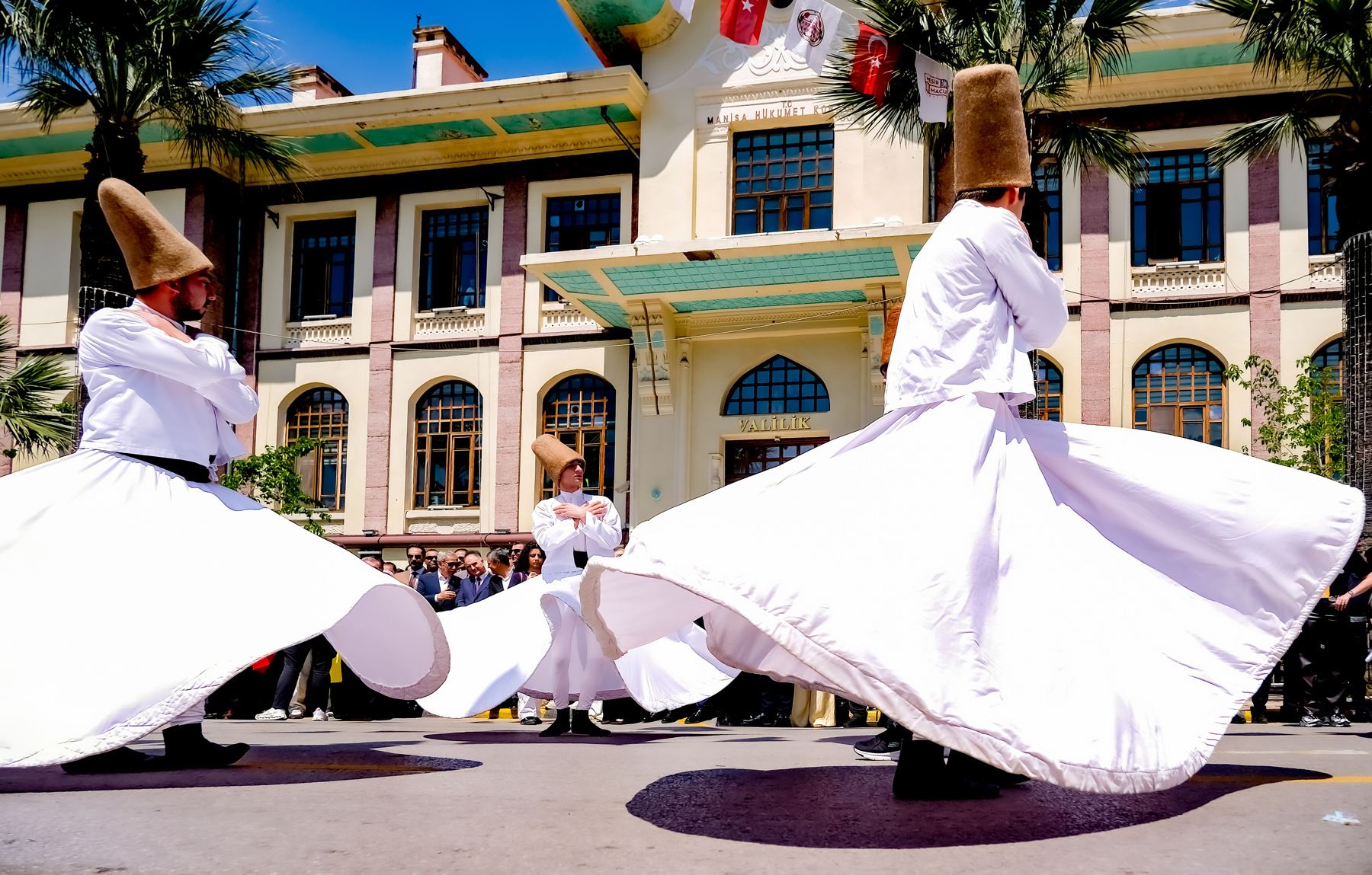 Whirling dervishes performing in white robes in front of a historic building